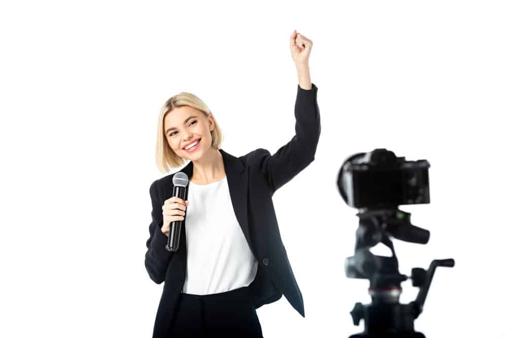 A broadcaster in front of the camera holding a mic