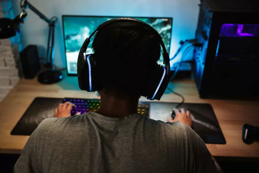 Back view of a teenage boy wearing headphones while playing online games.