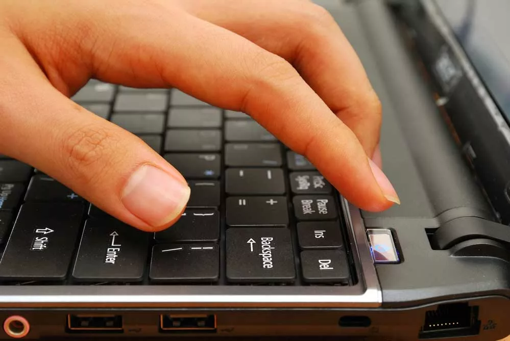 Finger pressing the power button on a laptop keyboard
