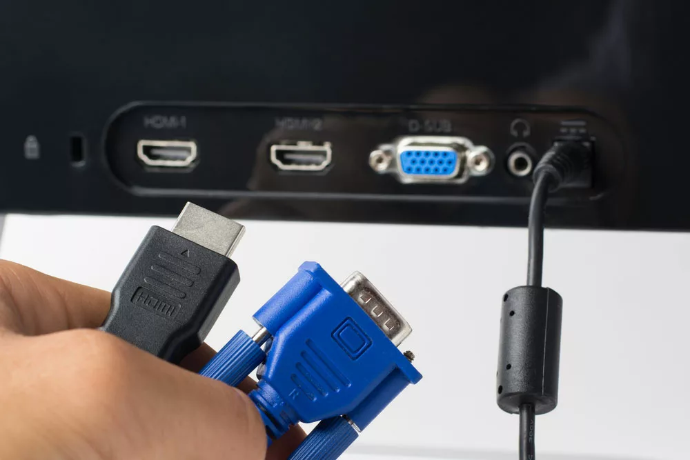 A hand holding an HDMI cable and a VGA cable.